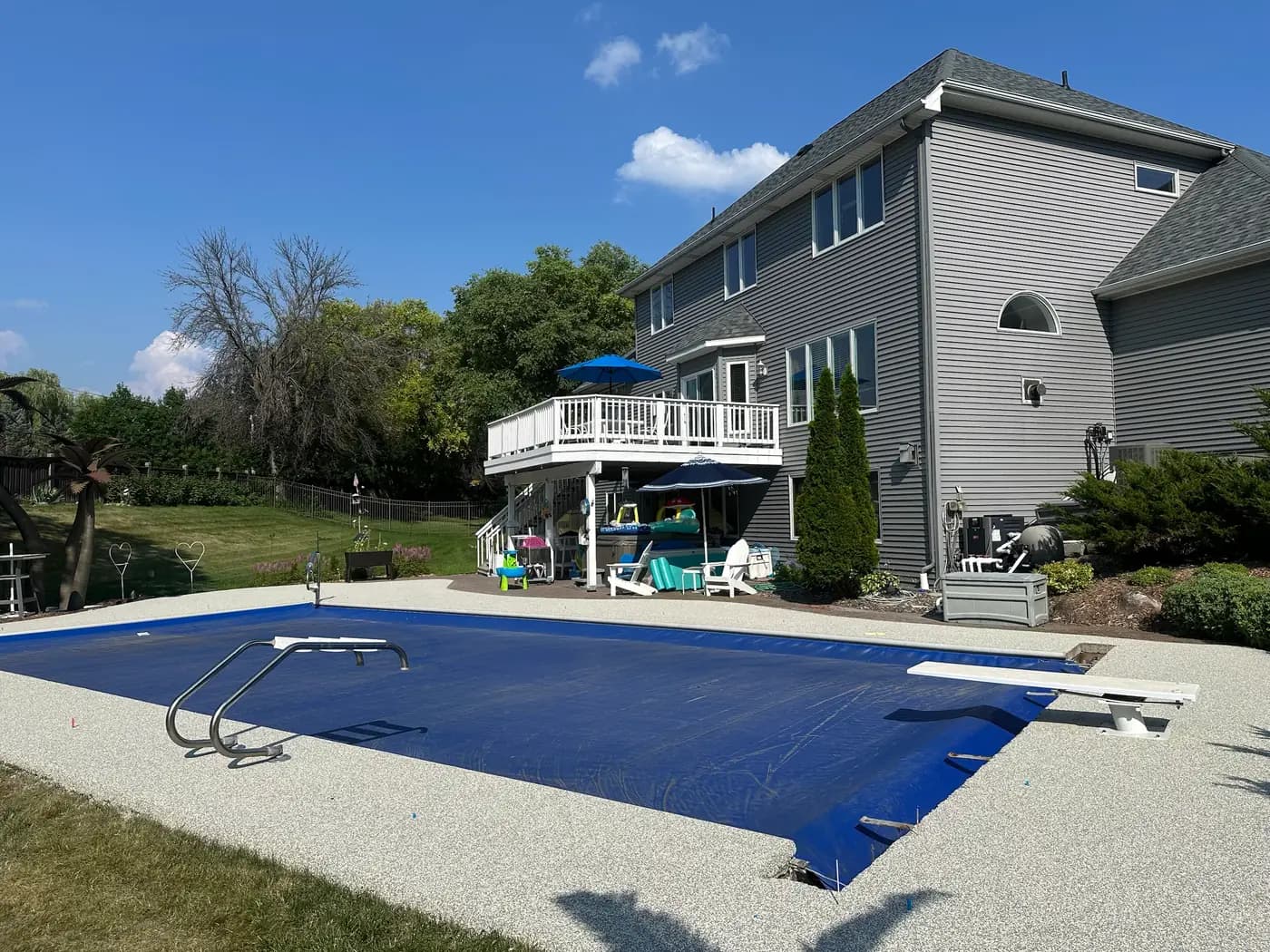 Light gray RevaFlex surround beside a covered pool with a diving board, installed by WAMS
